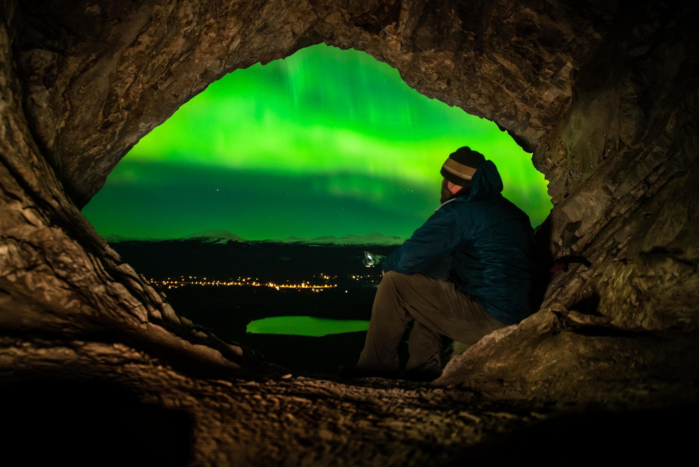 A man watches the northern lights over the city of Whitehorse from a cave.