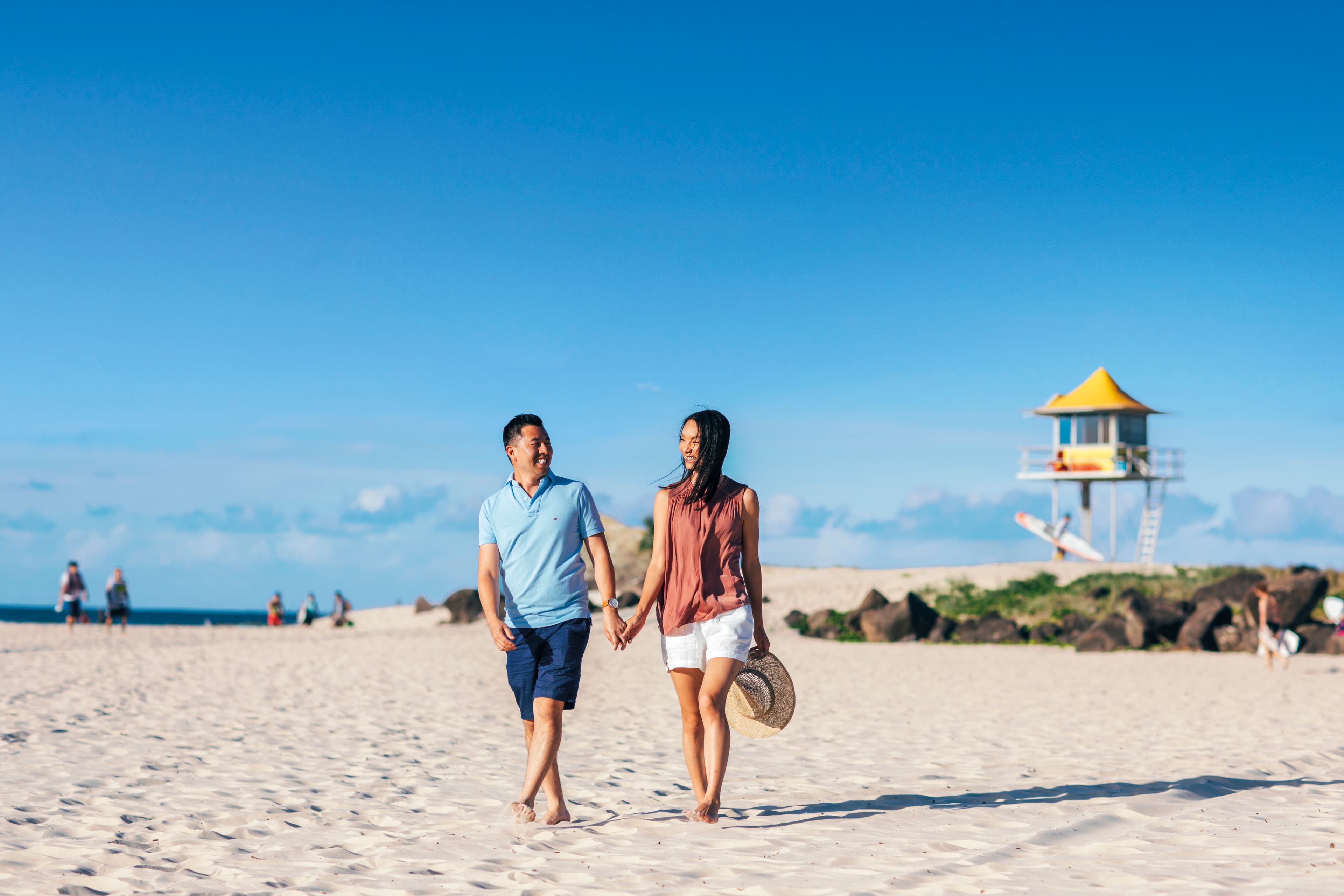Chinese couple walking along the beach with the skyline in the background